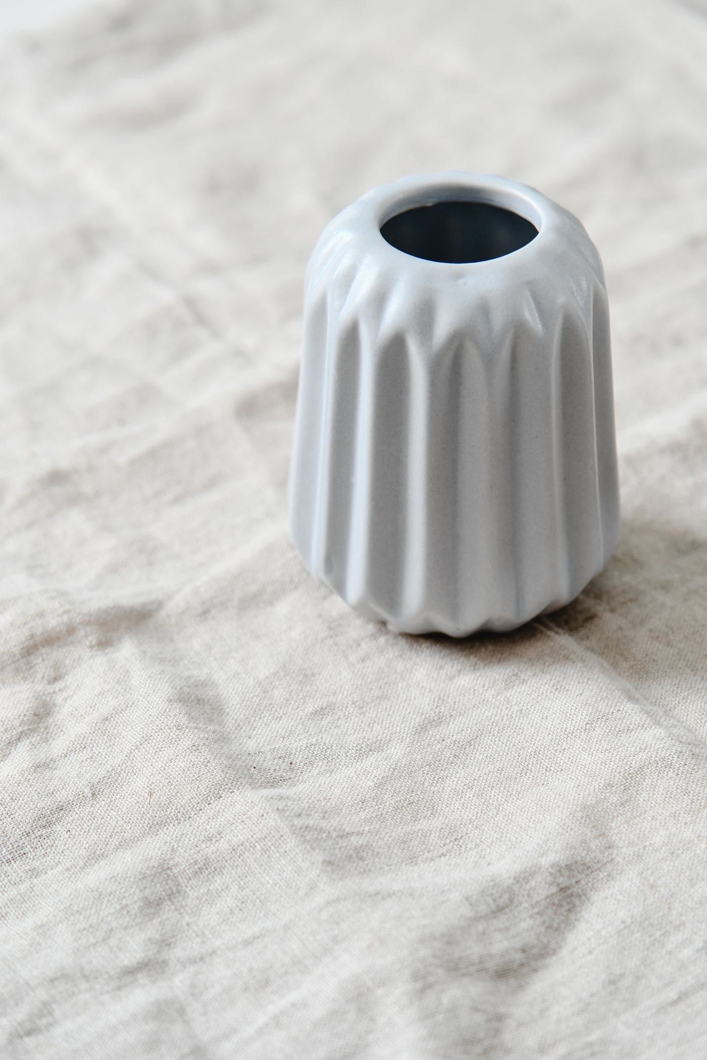 Weiße gerippte Vase auf hellem Stoff